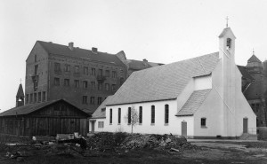 Zwei Kreuzkirchen nebeneinander: Am Ort der heutigen Kreuzkirche steht 1950 noch die Schweizer Militärbaracke, die als Notkirche diente - daneben die am 16. April 1950 eingeweihte »Bartning-Notkirche«. Im Hintergrund ist das Pfarrhaus mit notdürftig repariertem Dachstuhl zu sehen.